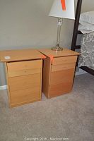 Two wooden Scandinavian style nightstands side by side with a clear glass lamp on the right nightstand.