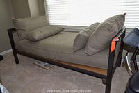 Daybed with dark metal frame and beige fabric cushions, side view showing cushion arrangement and frame design.