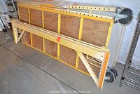 Folded metal scaffold with yellow wooden platform and large caster wheels, stacked for storage.