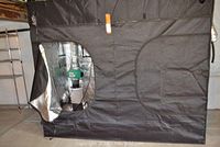 Exterior of black fabric tent with zipped entry partially open showing reflective interior.