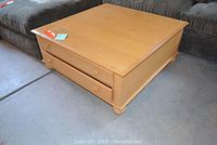 Wood coffee table with drawers on side, square knobs, and ball feet on base, placed on carpet near dark sofa.