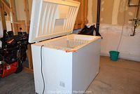 White GE chest freezer with lid open, showing interior basket and power cord along side.