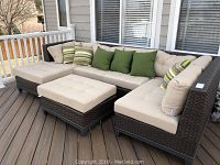 Angled view of L-shaped brown woven resin rattan sectional with beige cushions and green and striped throw pillows