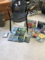 View of two black metal outdoor chairs, tennis instructional CDs laid out on floor, assorted kids games near chairs.