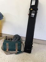 Yamaha black sound bar standing against a wall with attached cables and small remote control. Sony video camera and green carrying bag seen beside it.
