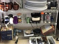 Close view showing more details of kitchen utensils, pasta machine box, LED bulbs box, stacked plastic platters, and assorted mugs and water bottles.