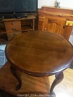 Round wooden side table with smooth surface and carved legs in living room setting.