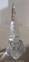 Full view of clear crystal perfume bottle with the tall triangular stopper with pagoda temple engraving on back side visible.