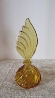 Full view of vintage amber colored swirled glass perfume bottle with tall stylish leaf stopper standing on lace fabric.