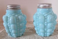 Pair of blue glass shakers with guttate pattern and metal caps displayed side by side on lace fabric.