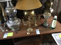 Silver-colored large oil hurricane lamp with glass chimney on a wooden table with brass candelabra and candle snuffer