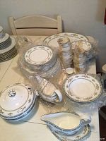 Wide view of Wedgwood bone china pieces including stacked plates, cups, gravy boats, and covered serving bowl on table.