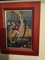 Framed print titled 'Popular Aviation' showing an airplane flying with a 25-cent price marking, framed in reddish wood.