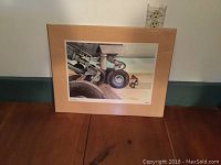 Framed print showing a close-up of airplane landing gear with a person crouching nearby, mounted on beige mat board.