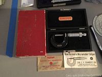 Starrett micrometer in black velvet-lined case with red outer box, manual, and wrench placed on a gray table.