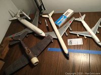 Overview of five model airplanes including three plastic JAL models, one delicate paper airplane, and one boxed model kit.