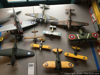 Top-down view of 10 assorted hand-assembled and hand-painted military model airplanes on table.