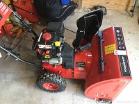 Side view showing red steel auger housing, adjustable chute and pneumatic tire
