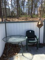 Full set including table, chair, umbrella and base outdoors on wood deck near white fence.