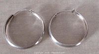 Pair of sterling silver hoop earrings laid flat showing full circular shape and smooth polished surface.