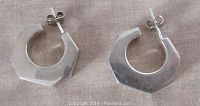 Pair of vintage sterling silver earrings shown side by side on fabric background, geometric faceted hollow hoop shape.