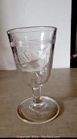 Full view of clear glass footed goblet showing shape and embossed cardinal design