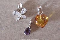 Photo showing three small sterling silver pendants and charm: heart-shaped amber pendant, cubic zirconia butterfly pendant, and small amethyst teardrop charm.