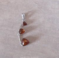 Front view of the vintage sterling silver pendant showing three triangular amber stones in a modernist curved silver setting.