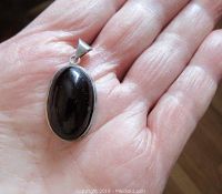 Front view of oval black onyx stone polished and set in sterling silver pendant held in palm.