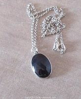 Photo showing oval dark labradorite cabochon pendant with attached sterling silver chain on fabric background.