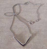 Image of the V shaped sterling silver pendant attached to the curb chain laid flat on a fabric background, with a visible spring ring clasp.