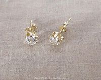Pair of small clear cubic zirconia stud earrings set in 10K yellow gold with box clasp backs, lying on a flat surface showing front and side details of setting and stones.