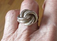Ring worn on finger showing woven infinity knot design and size relative to finger.
