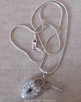Sterling silver heart padlock pendant with cubic zirconia, key charm, and 16-inch snake chain with lobster claw clasp laid out on surface.