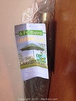 Green 6 Ft Bistro outdoor umbrella in closed position, with tag showing brand and details.