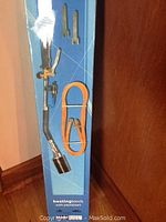 Heating torch with attached orange hose inside original packaging alongside two wrenches.