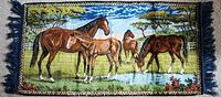Full view of vintage decorative horse carpet rug showing horses grazing near a stream in a field under a blue sky with fringed edges.