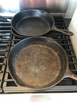 Photo of two round cast iron skillets stacked on a gas stove showing cooking surfaces and wear marks.