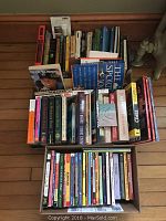 Box and loose books of various sizes and types arranged upright and stacked, showing a mix of children's and adult books, mostly hardcover and softcover.