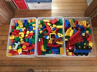 Three plastic bins filled with various colorful Duplo blocks, figures, and accessories on wooden floor.