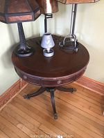 Photo showing the full pedestal table with several lamps on its surface, displaying the round tabletop and carved apron details.