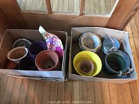Two cardboard boxes containing a total of 13 flower pots including ceramic and tin, of various colors and sizes between 4 and 8 inches.