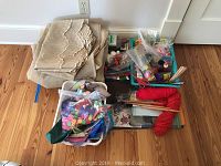 Photo of beige curtain panels folded neatly on wooden floor beside various arts and crafts supplies in containers and bags.