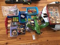 Overview of lot showing collectible pogs in a display case, wooden figures, baseballs, beanbag, green airplane toy, and assorted smaller toys.