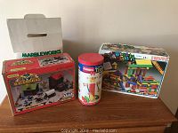 Collection of vintage toys including OK Corral, Tinkertoy, Wood Builders, and Marbleworks boxes on a wooden surface.