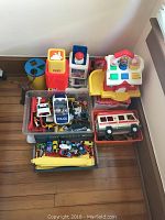 Multiple children's toys including Little Tikes shape sorter house, various toy cars and figures in plastic storage bins, Fisher Price turn wheel toy
