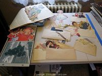 Full display of paper doll sets, envelopes with paper cutouts, and loose paper doll figures and clothes on table.