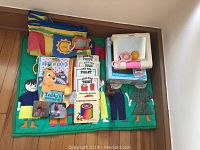 Top-down view of fabric play mats with cartoon children, children's books, and Fisher-Price baby toy.