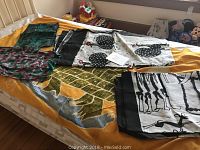 Five pieces of African fabrics arranged spread on a bed showcasing different colors and patterns including large reptile print, black circular motifs on white, and others.