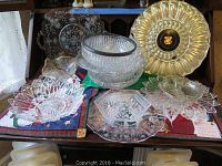 Several clear crystal and cut glass serving pieces including bowls and dishes with detailed cut patterns, arranged on holiday-themed tablecloths.